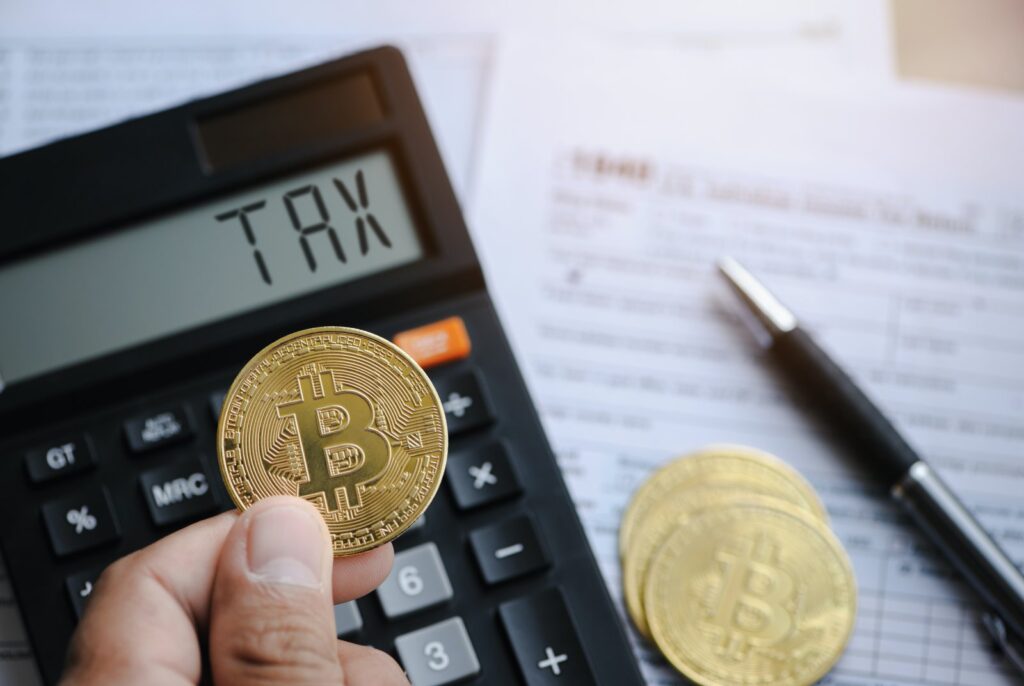 A calculator with tax written, crypto coins, and tax form, symbolizing crypto taxation