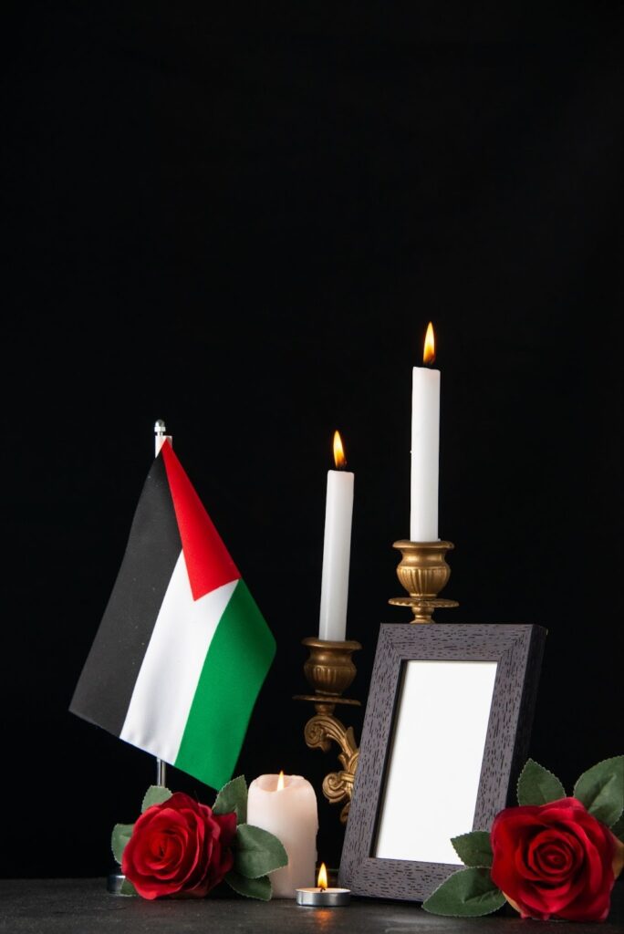 Burning candles with Palestinian flag and flowers on a dark surface