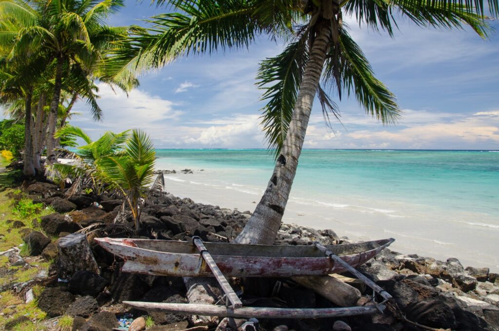Old wooden boat on the shore surrounded by the sea and palm trees in the Savai'i island, Samoa.