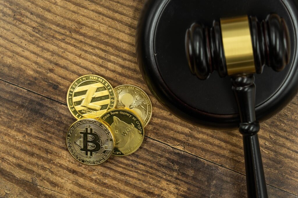 A pile of cryptocurrency, including Bitcoin, Litecoin, Dogecoin, and Ethereum, lying beside a judge’s gavel.