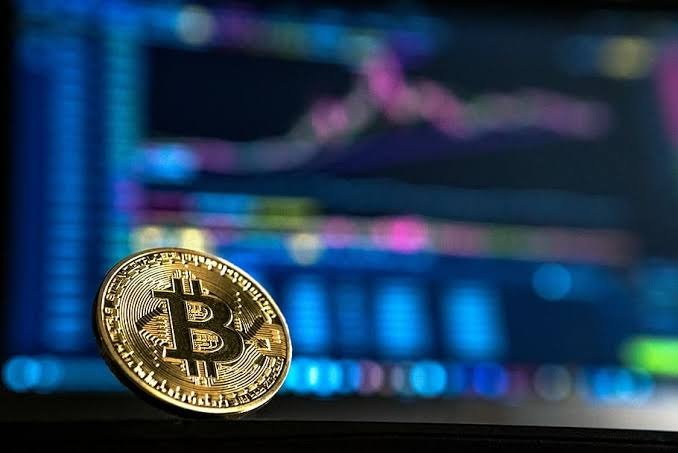 Bitcoin in front of a laptop with a blurred cryptocurrency chart on display 