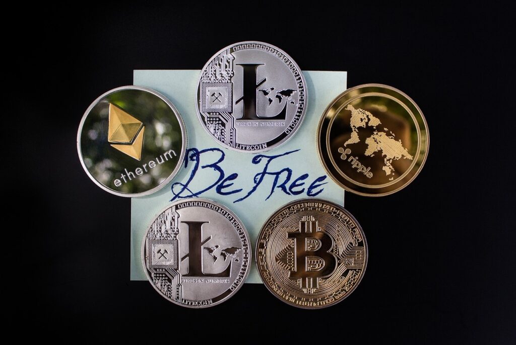 Five different cryptocurrency coins arranged around a blue sticky note with the inscription "Be Free.”