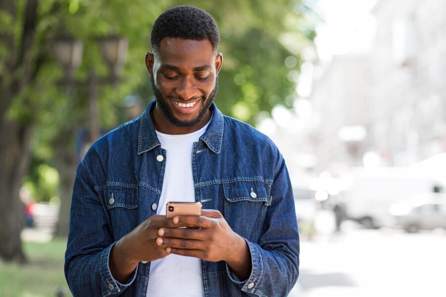 A man smiling while using a smartphone outdoors