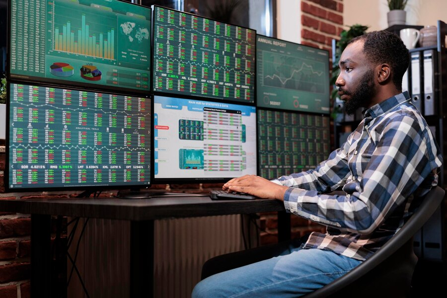 Stock trader analyzing multiple monitor screens with market data