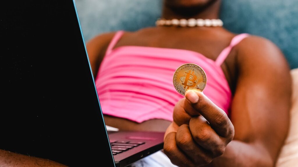 Close-up detail of a hand holding a Bitcoin coin of a black transgender unrecognizable person while shopping online.