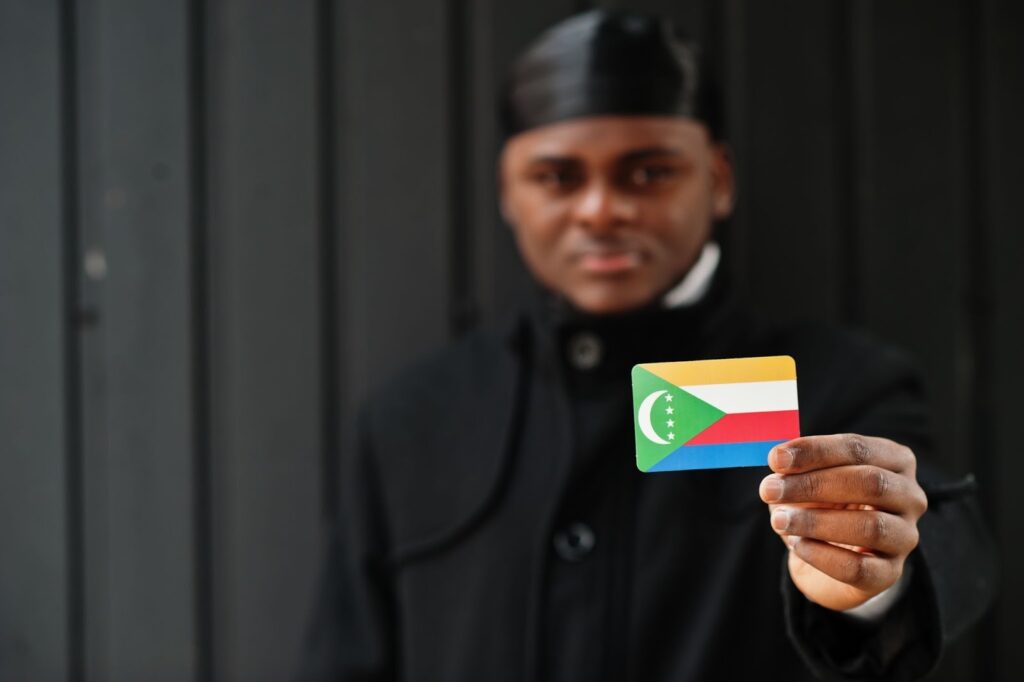 African man wearing black durag holds Comoros flag at hand in an isolated dark background.