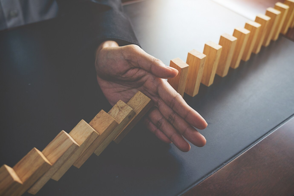 Close-up of a businesswoman's hand stopping falling domino blocks on a table.