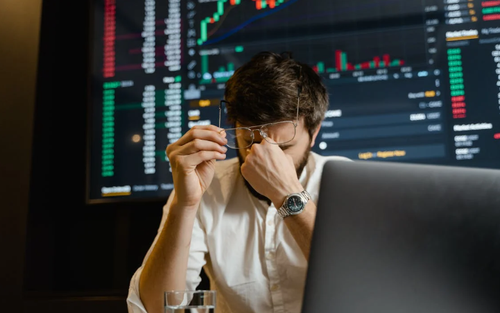 A devastated man sitting across a laptop with trading chart behind him