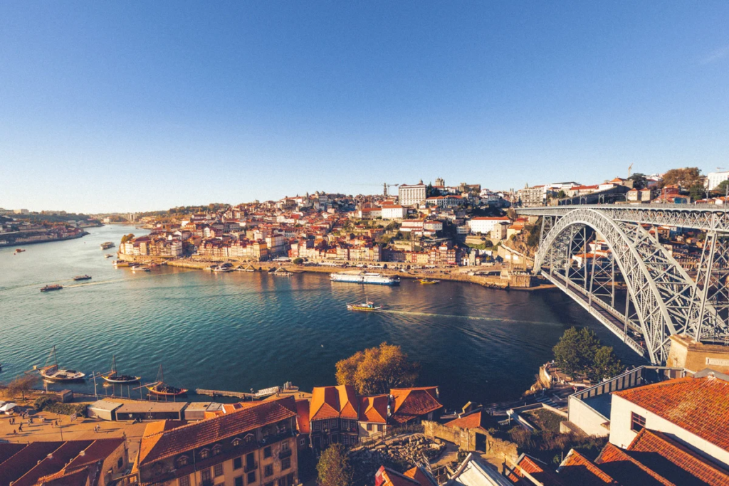 Panoramic view of Porto’s historic riverside along the Douro River, featuring traditional hillside buildings, boats on the water, and the Dom Luís I Bridge connecting Porto and Vila Nova de Gaia.